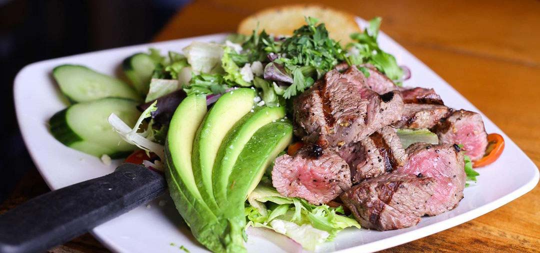 White plate with steak, salad, and avocado.