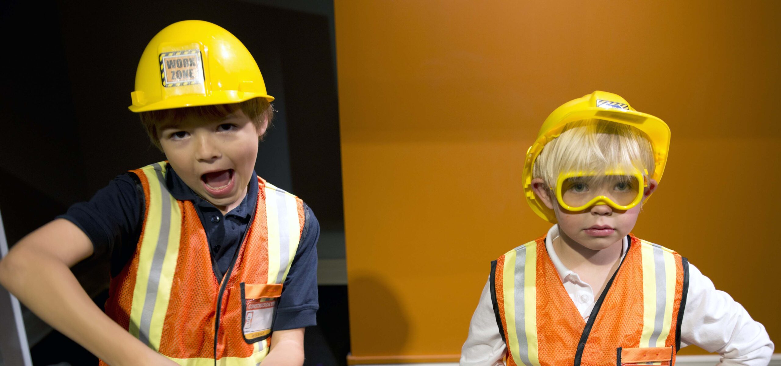 Young boys dressed up in toy construction gear like hardhats and vests.