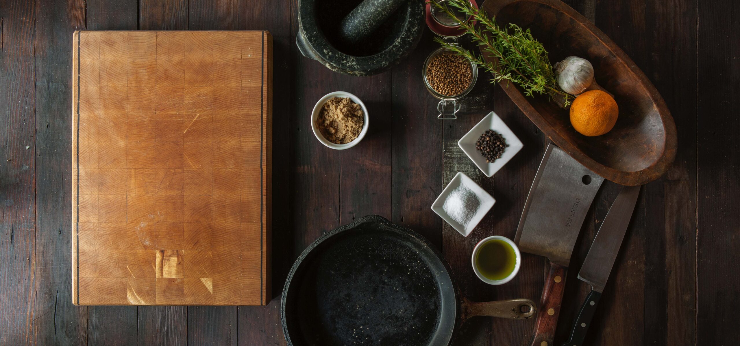 Birds-eye view of a kitchen counter with wood cutting board, herbs, and bowls.