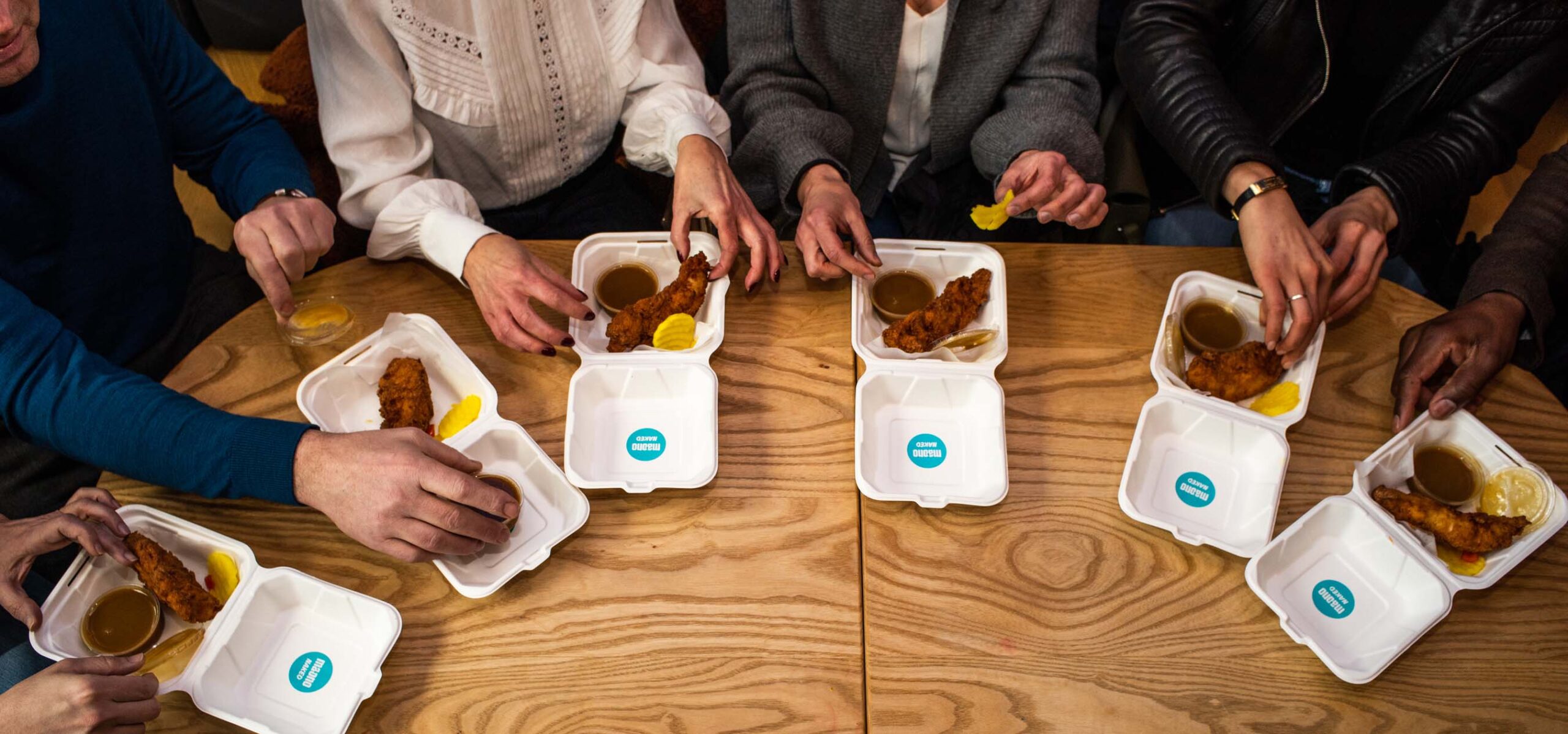 Overhead view of people eating from to go sandwich boxes.