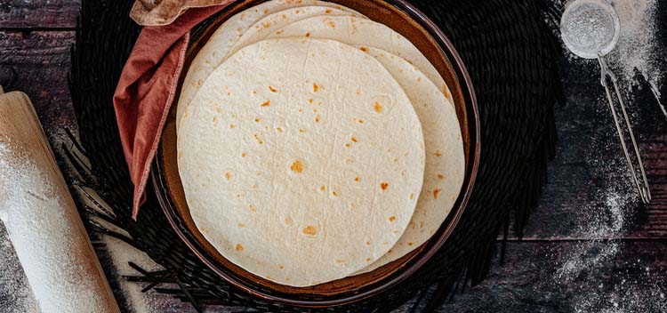 Dish with flour / masa tortillas next to a rolling pin.