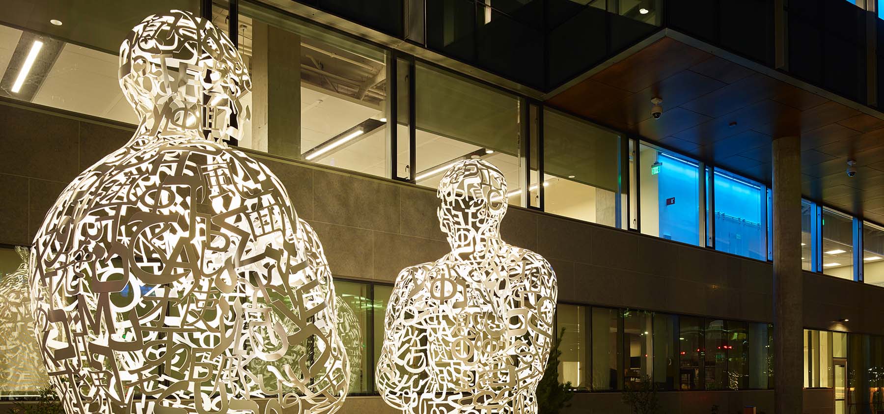 Two frames of modern outdoor art that look like people sitting and holding their knees.