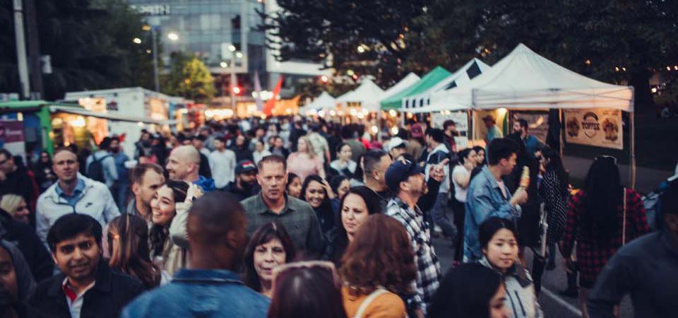 Photo of patrons walking among outdoor market vendor tents.