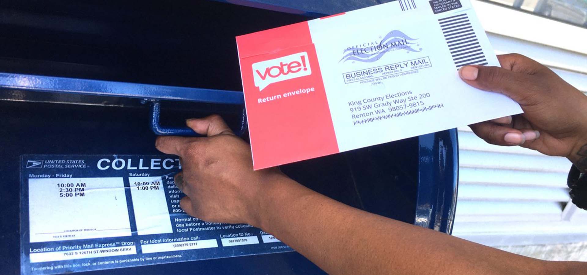 Person's hands mailing their ballot in a mailbox