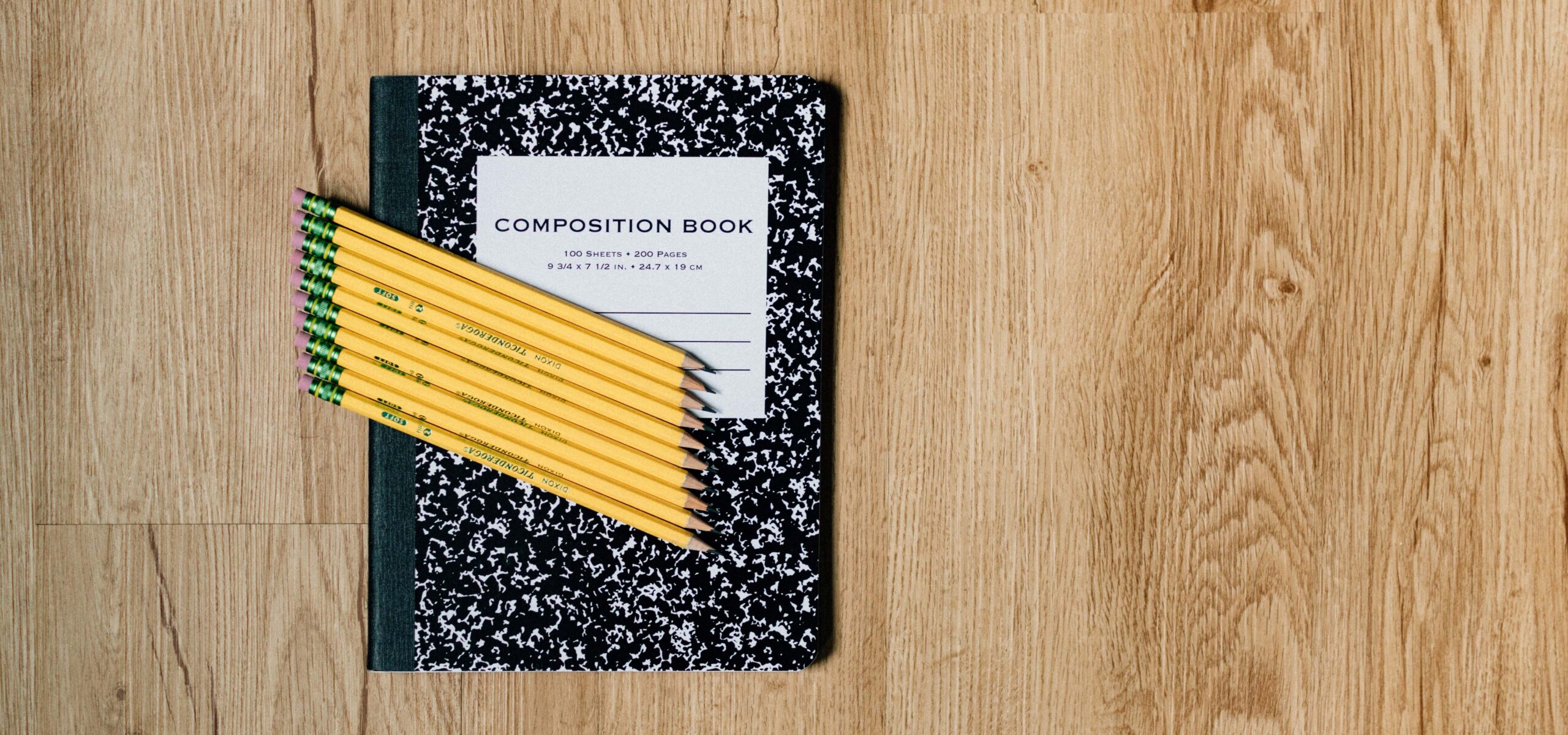 Wood desk top with black composition notebook and sharpened pencils.