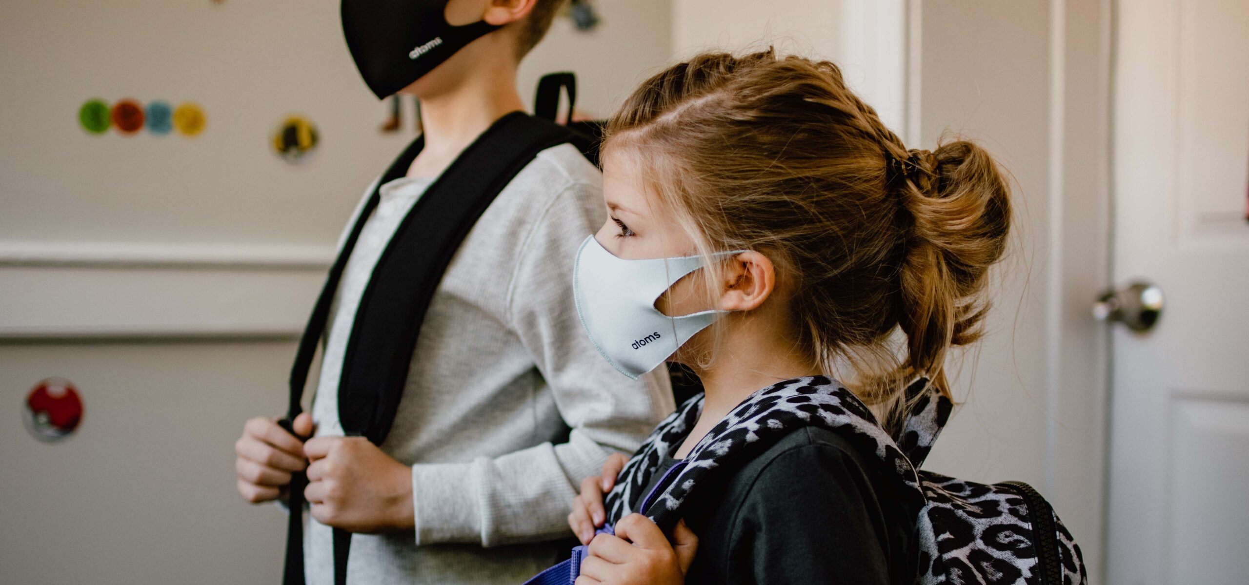 School-aged girl and boy with backpacks and masks on, appear ready to head off to school.