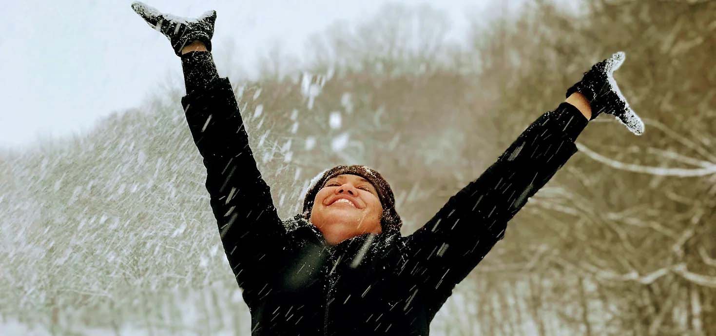 Girl with hands up in the air while snow falls down.