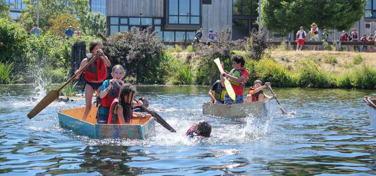 Kids rowing handmade boats in a lake for fun.