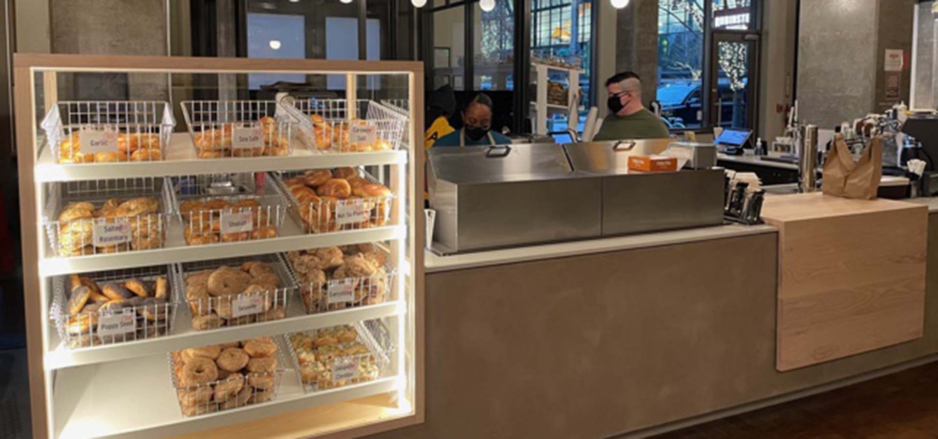 Store interior of a bagel counter with staff and baskets of bagels.