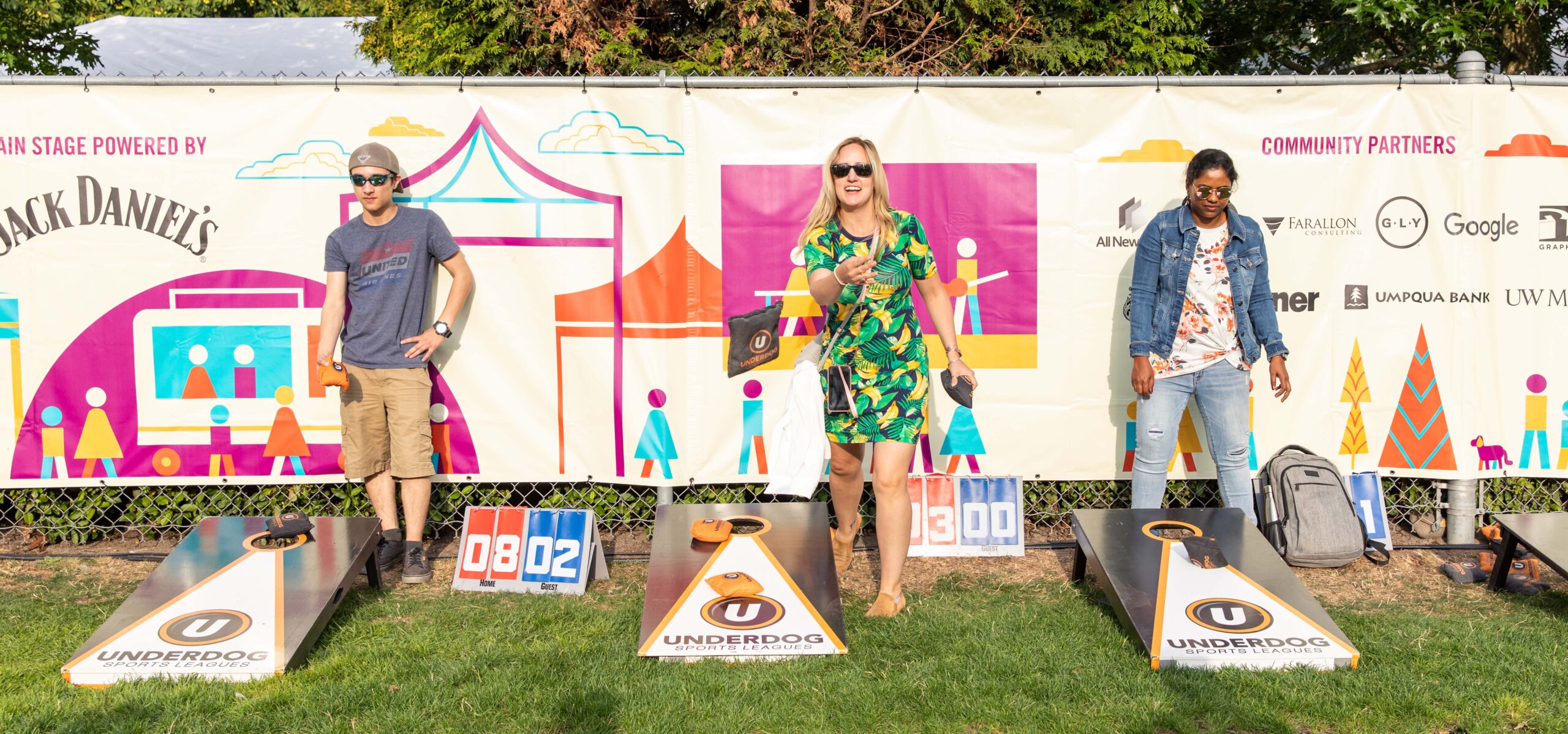 People playing corn hole bag toss games on a lawn.