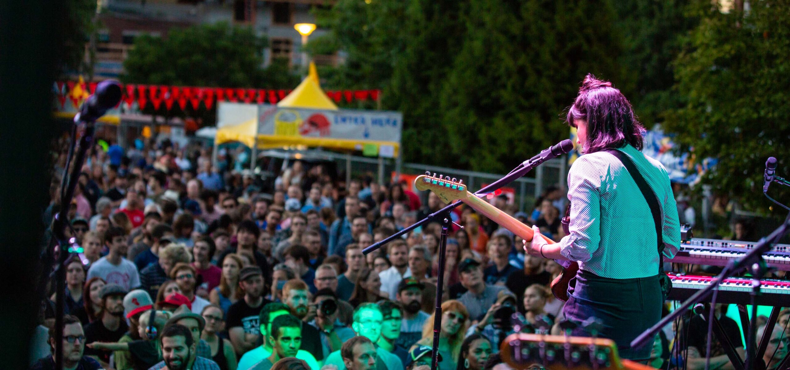 Woman in a band singing to a crowd at a festival.