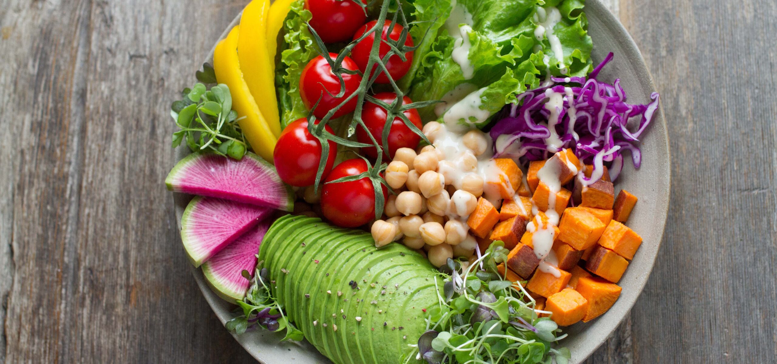 White bowl with colorful salad items such as carrots, tomatoes, and avocados.