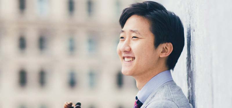 Asian American violinist, Sean Lee smiling and holding his violin.