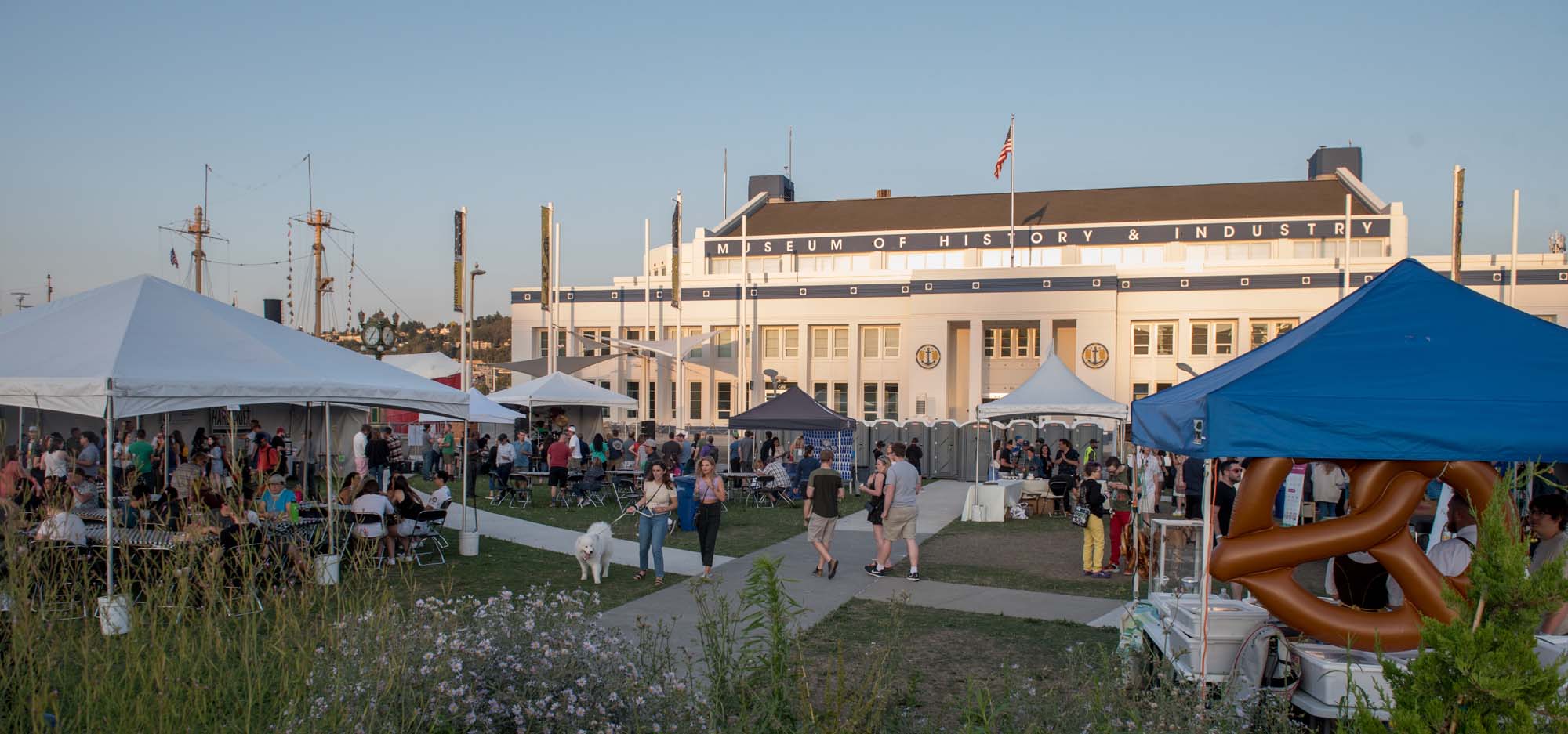 A cider festival with tents and patrons during a summer evening.