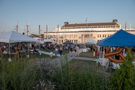 A cider festival with tents and patrons during a summer evening.