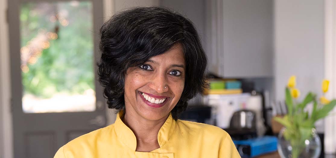 Woman smiling wearing a yellow chef's coat.