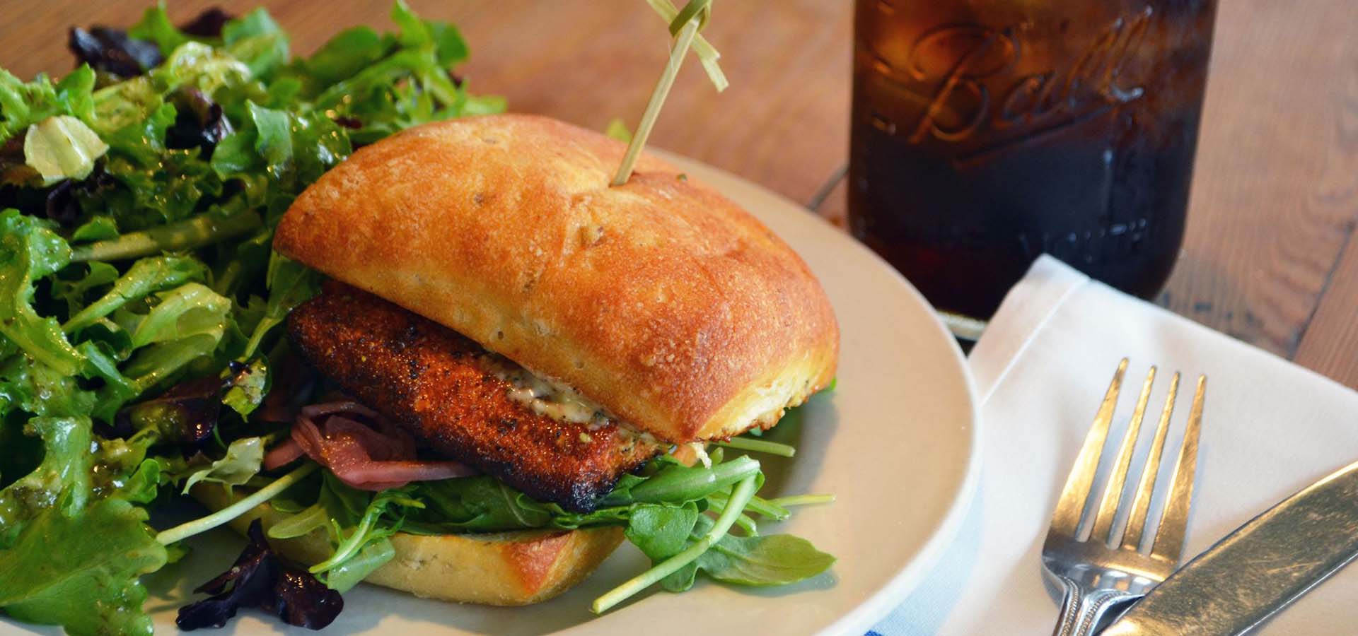 Grilled salmon sandwich with greens on a plate.