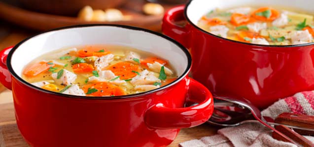 Red soup bowls filled with chicken noodle soup.