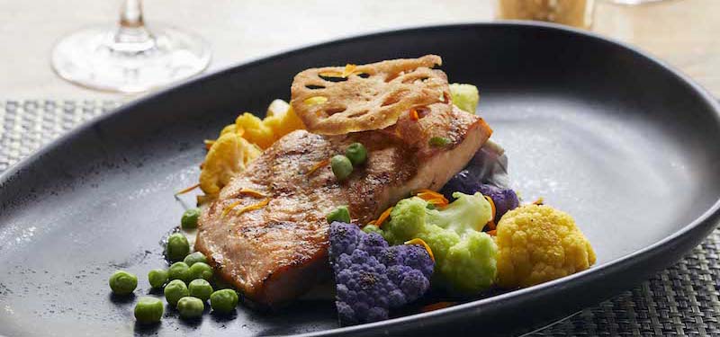 Plated salmon dish with colorful vegetables.