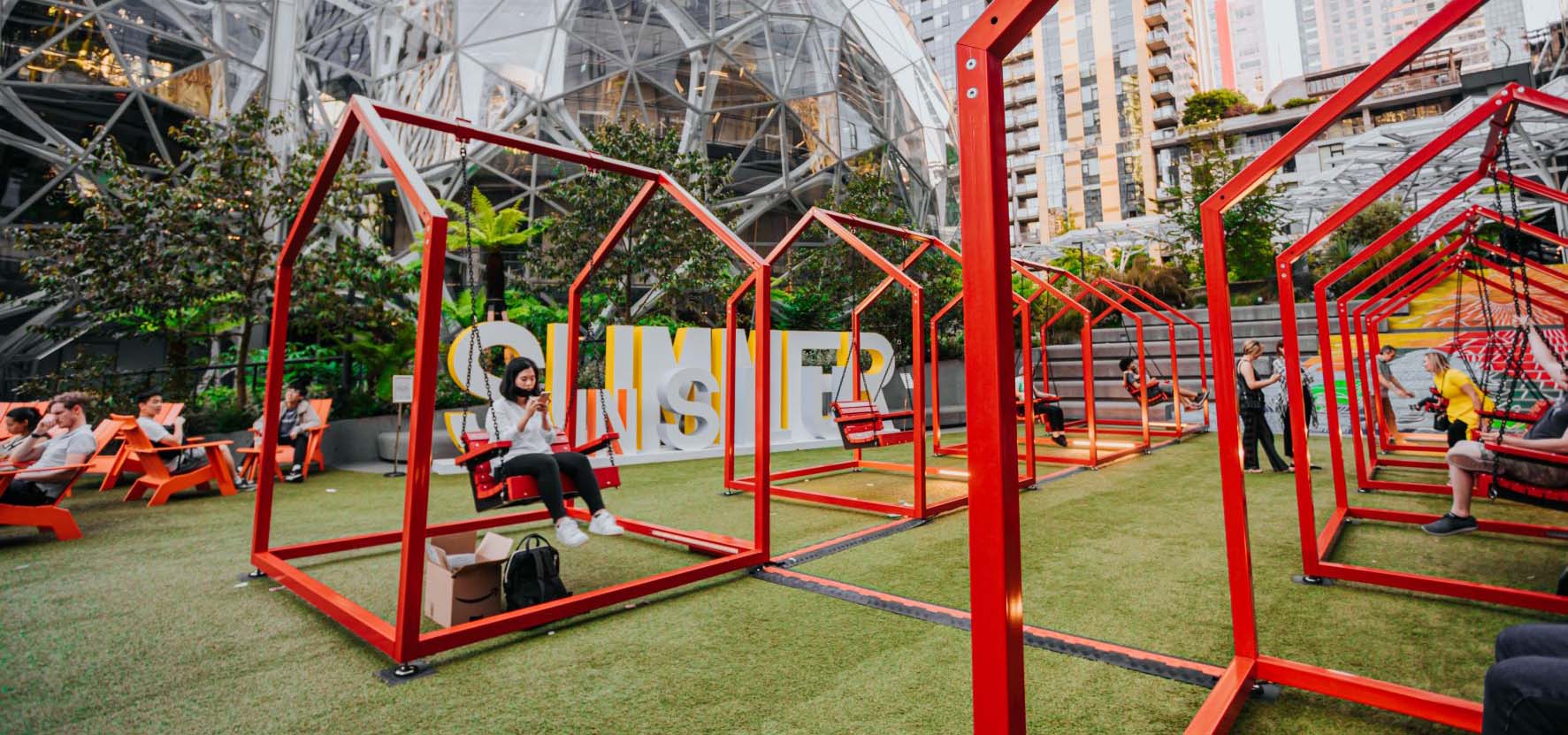 People swinging on outdoor interactive art designed after house porch swings.