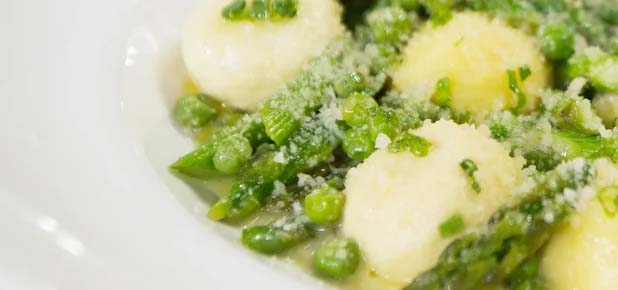 White plate filled with gnocchi, peas, and asparagus.