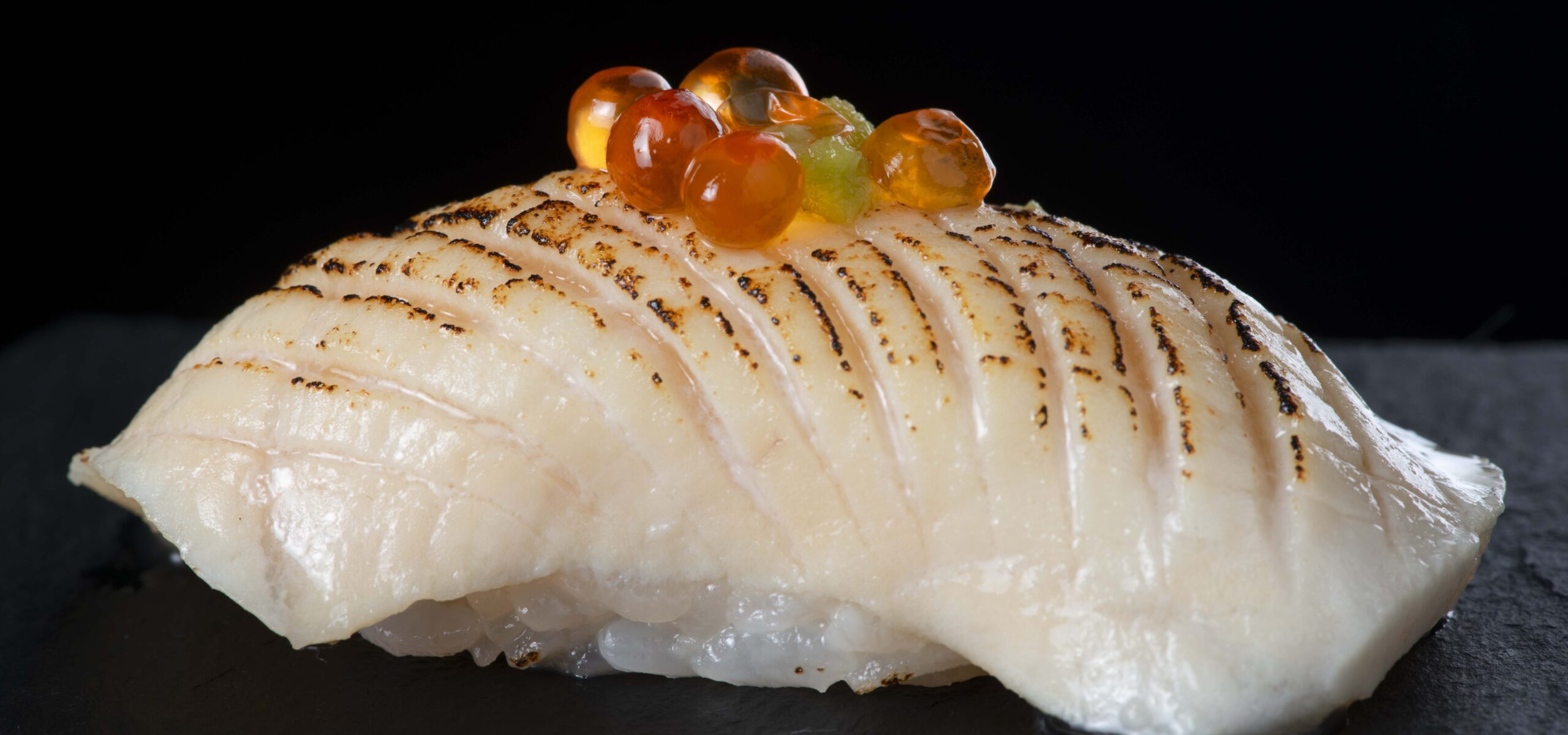 Up close photo of a white fish sushi topped with fish eggs.