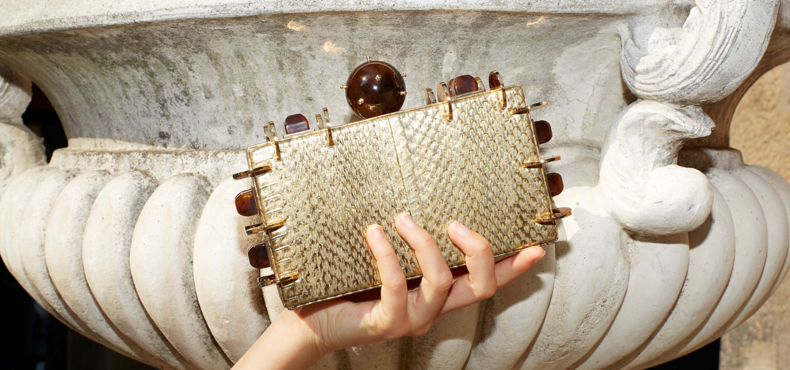 Hand holding a snake skin designer handbag in neutral tones.