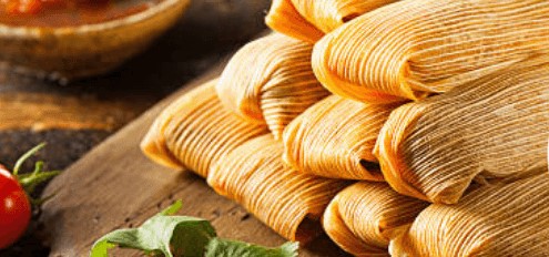 Cutting board filled with stacked tamales.