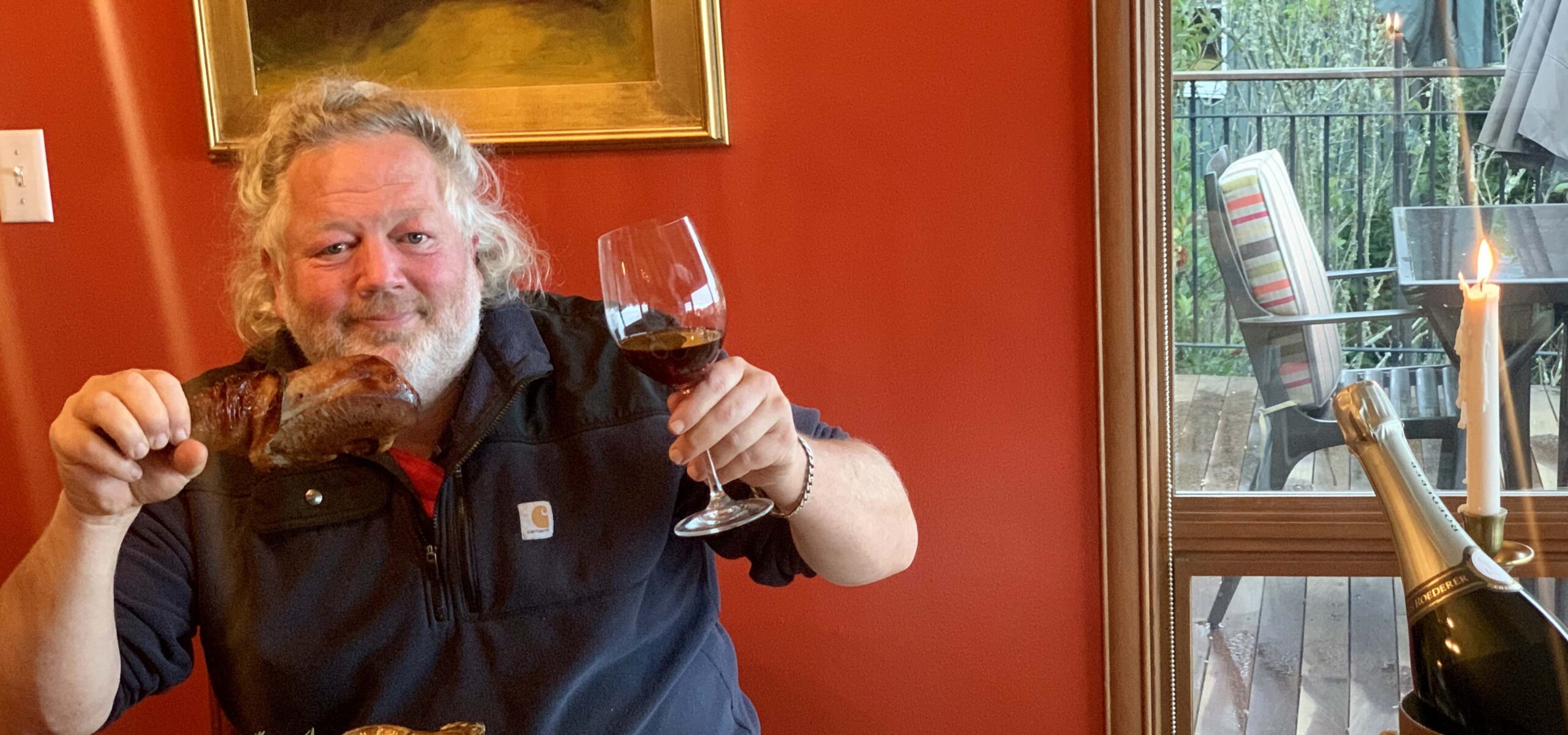 Chef Tom Douglas holding a turkey leg and glass of wine at a Thanksgiving table.