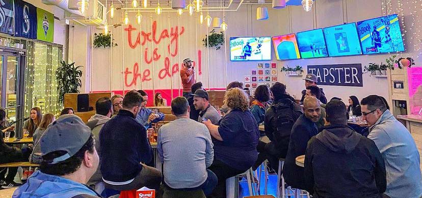 People gathered in a taproom listening to a comedian.