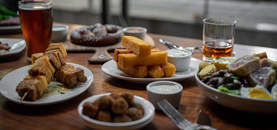 Table spread of happy hour snacks like fried tofu, soft pretzels, and olives.