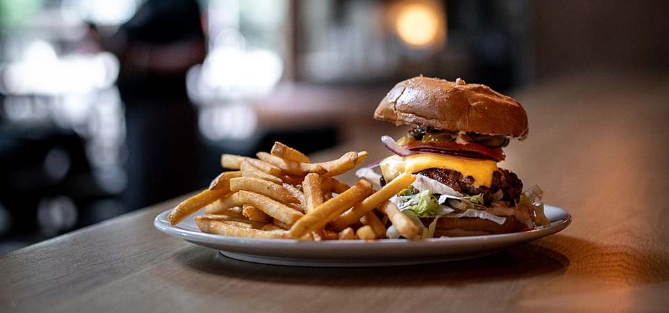 Gourmet burger plated with french fries on a bar counter.