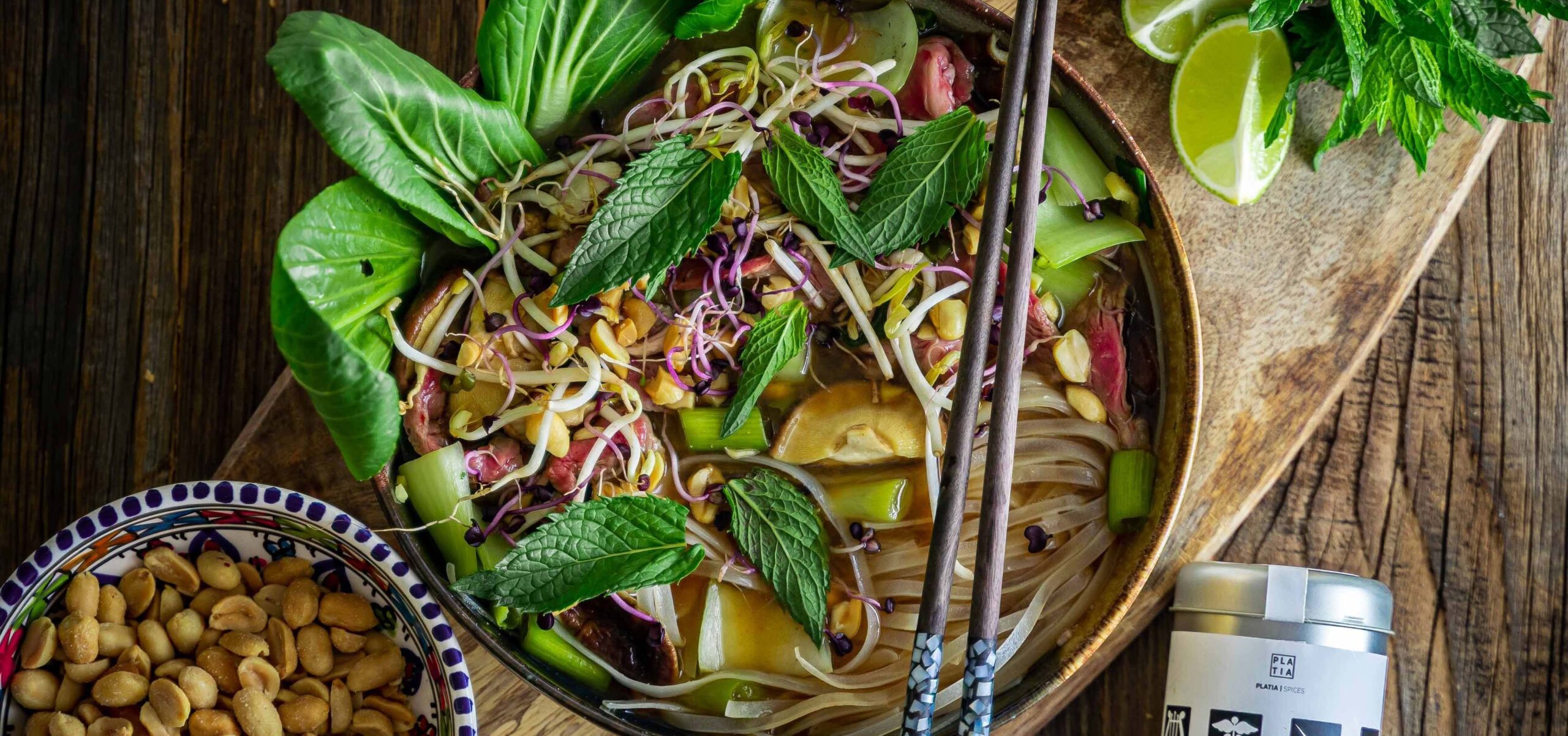 Bowl of Vietnamese noodles with basil on top and limes on the side.
