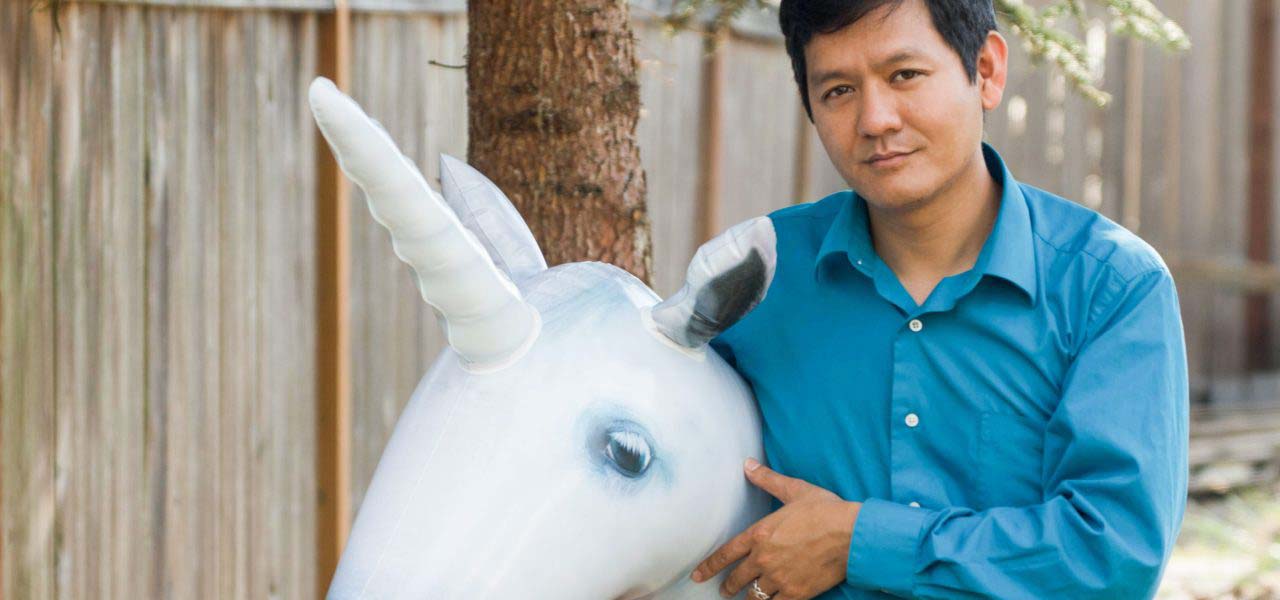 An Asian man holding a blow up toy unicorn.