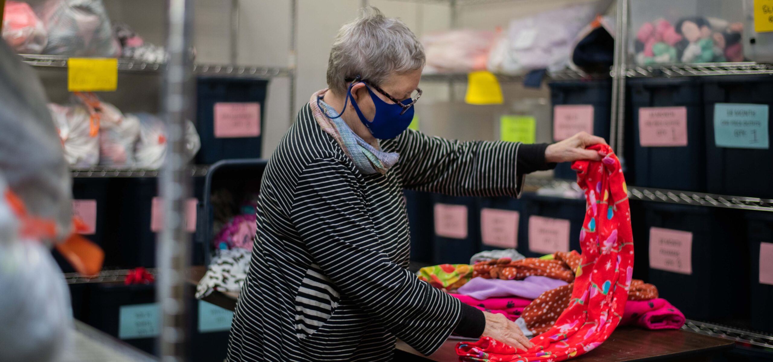 Elderly woman folding baby blankets in a storage facility.
