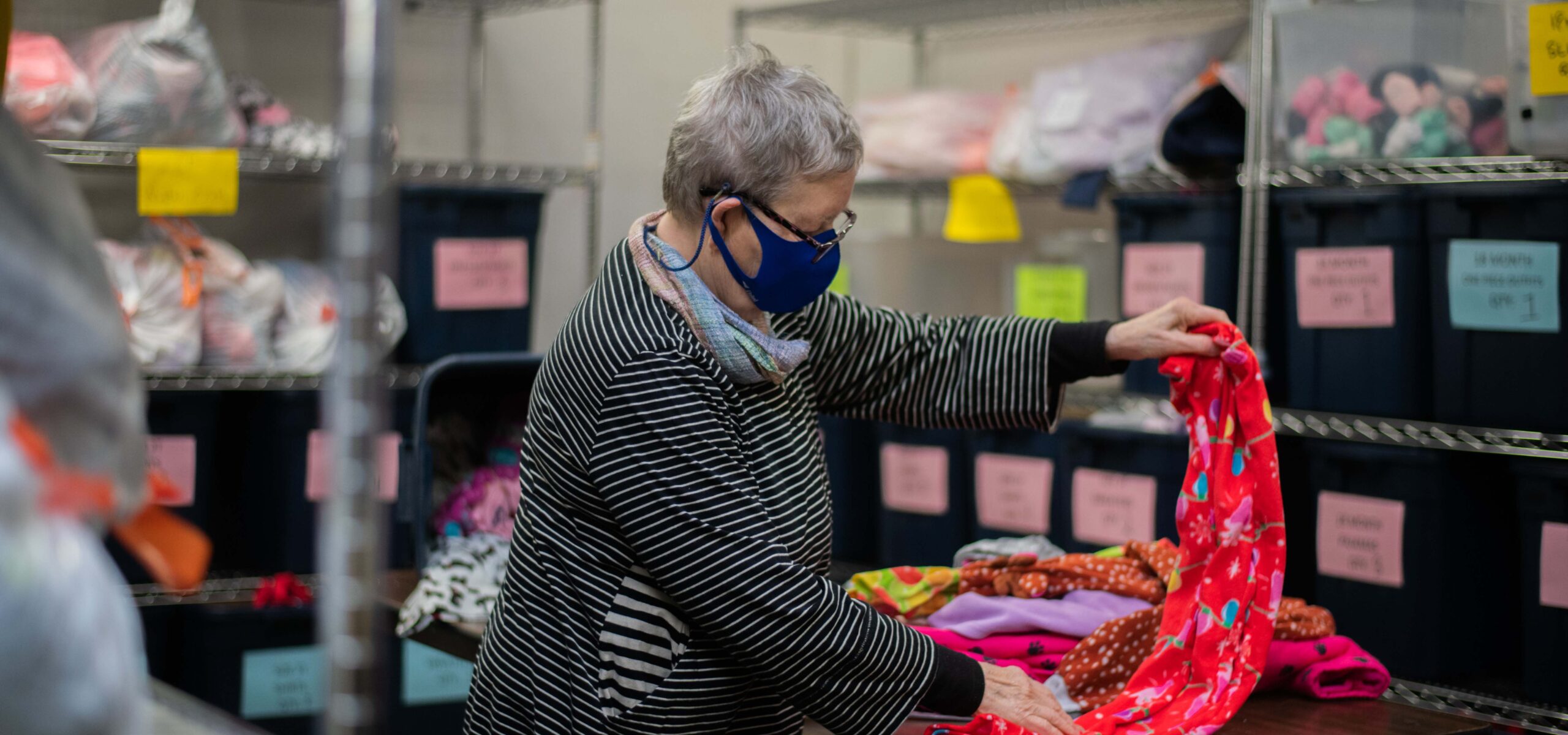 Elderly woman volunteer folding a red baby blanket.