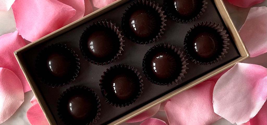 Box of chocolates surrounded by pink rose petals.