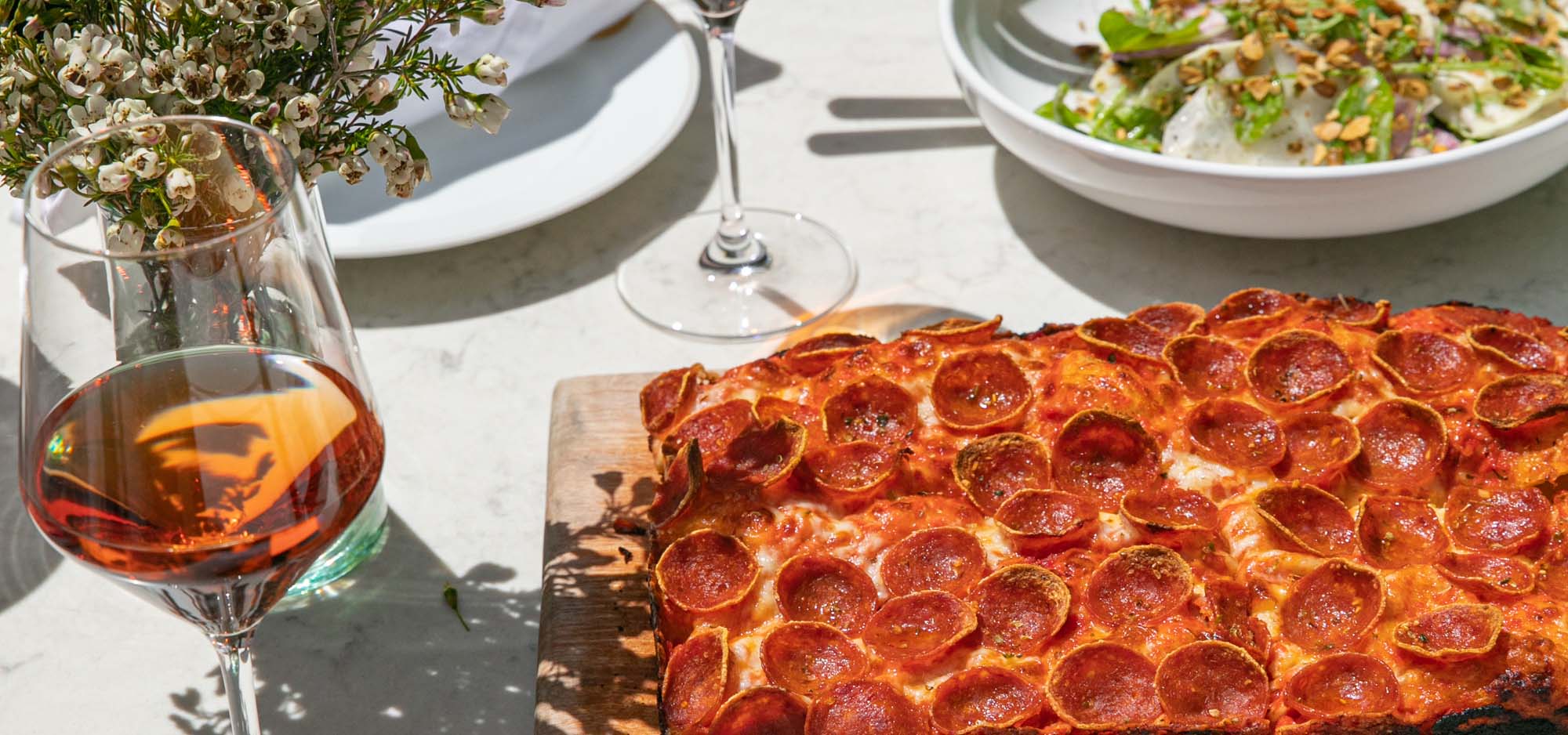 High end table setting with cutting board serving a deep dish pizza and bowl with Cesar salad.