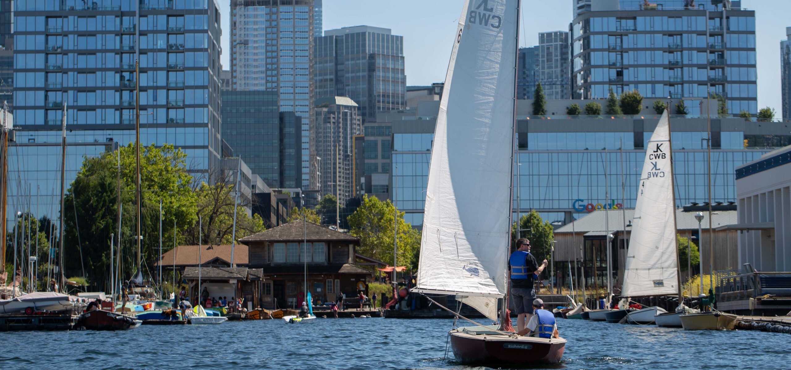 Two people on a sailboat on Lake Union with downtown Seattle in the background.