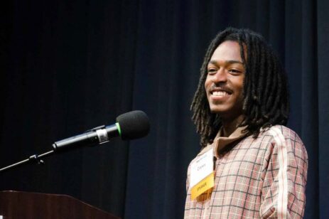 Man speaking and smiling at a podium with a microphone.
