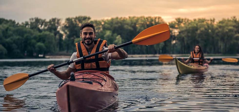 A man and woman kayaking on a lake at sunset.