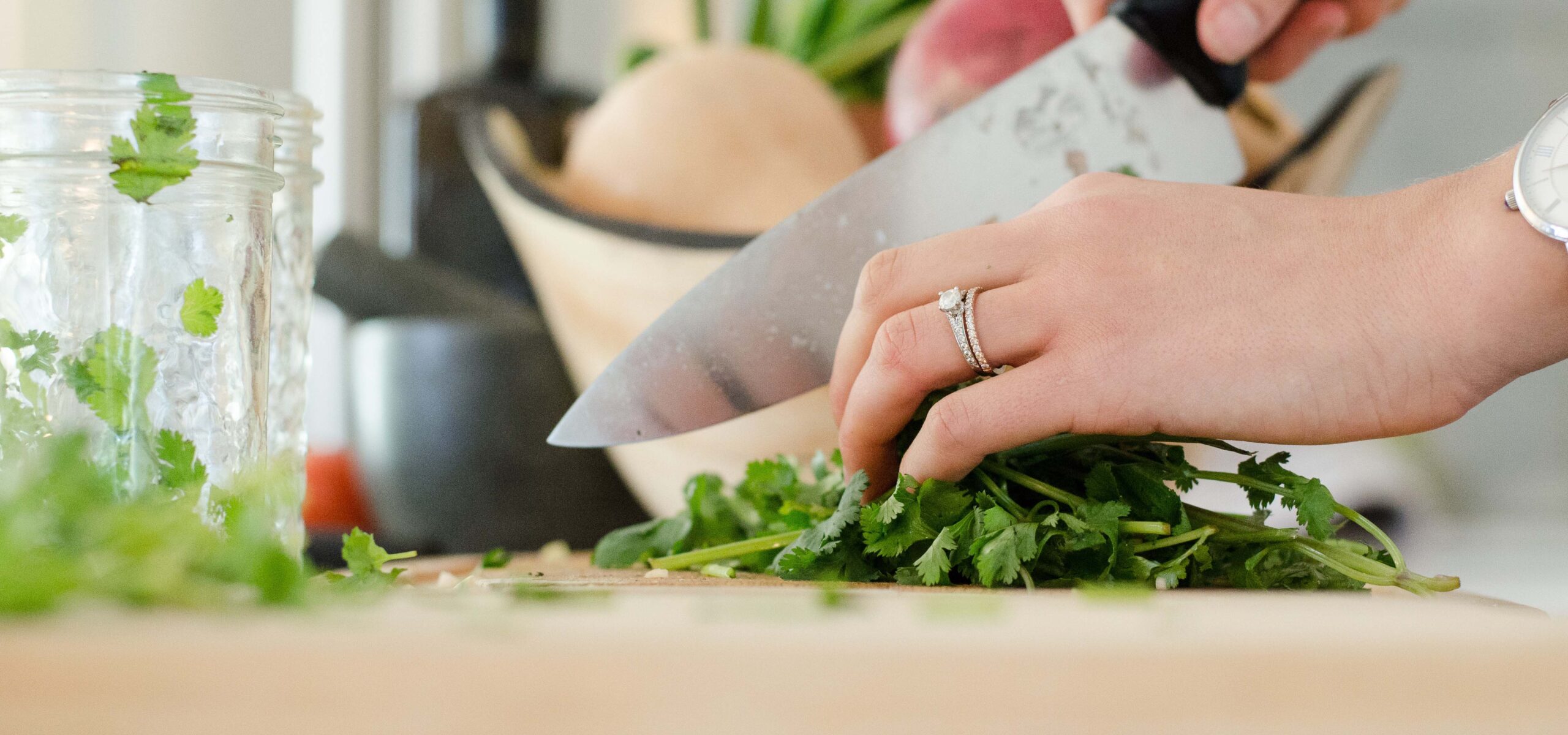 Woman's hands using a chef's knife to chop herbs on a wood cutting board.