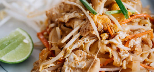 Plate of Asian noodles with vegetables and a side of limes.