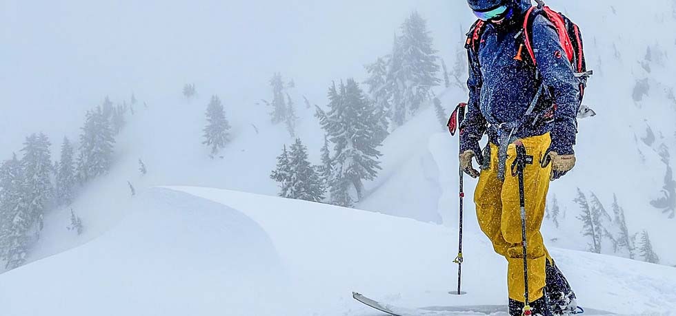 Man skiing stopped at the top of a mountain run, it's snowing.