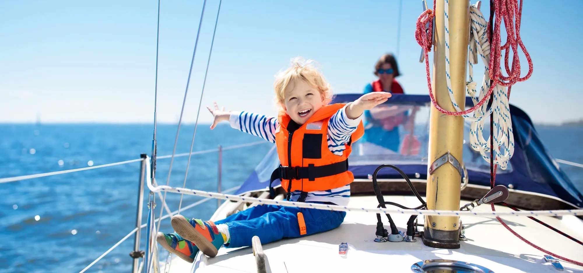 Young blonde child holding out arms like they are flying while sailing on a boat.