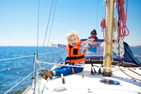 Young blonde child holding out arms like they are flying while sailing on a boat.