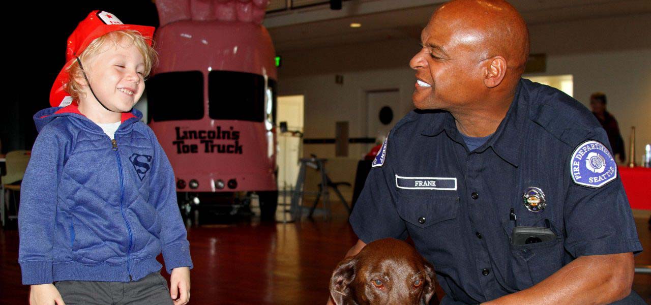 Fireman smiling at a boy in a fireman's hat.