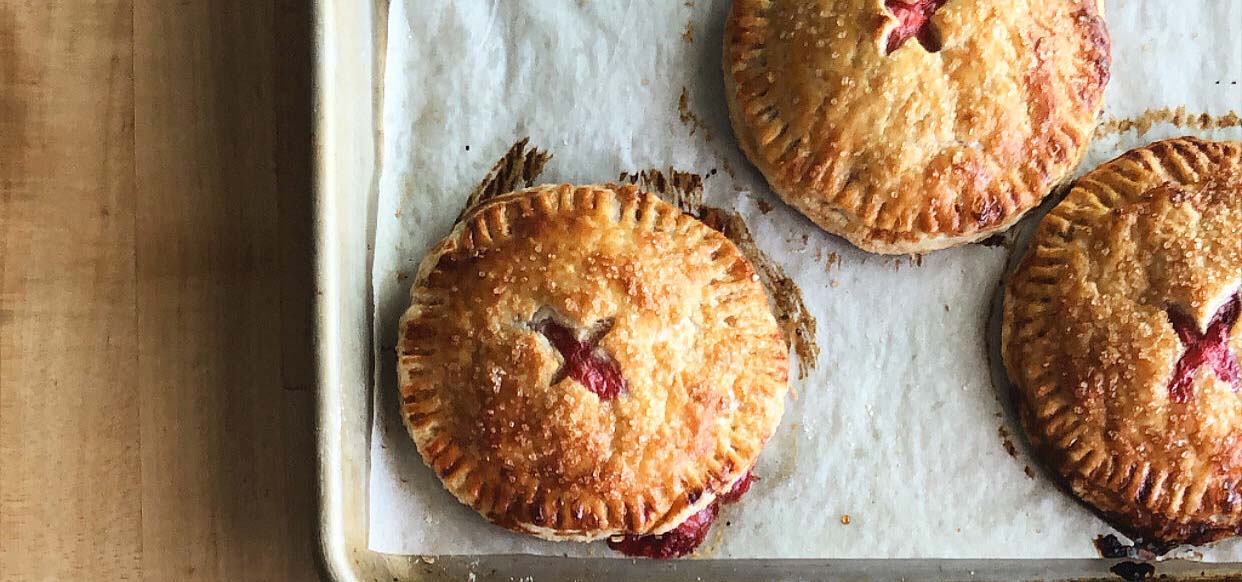 Round cherry hand pies on a baking sheet.