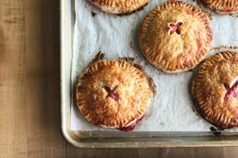 Round cherry hand pies on a baking sheet.