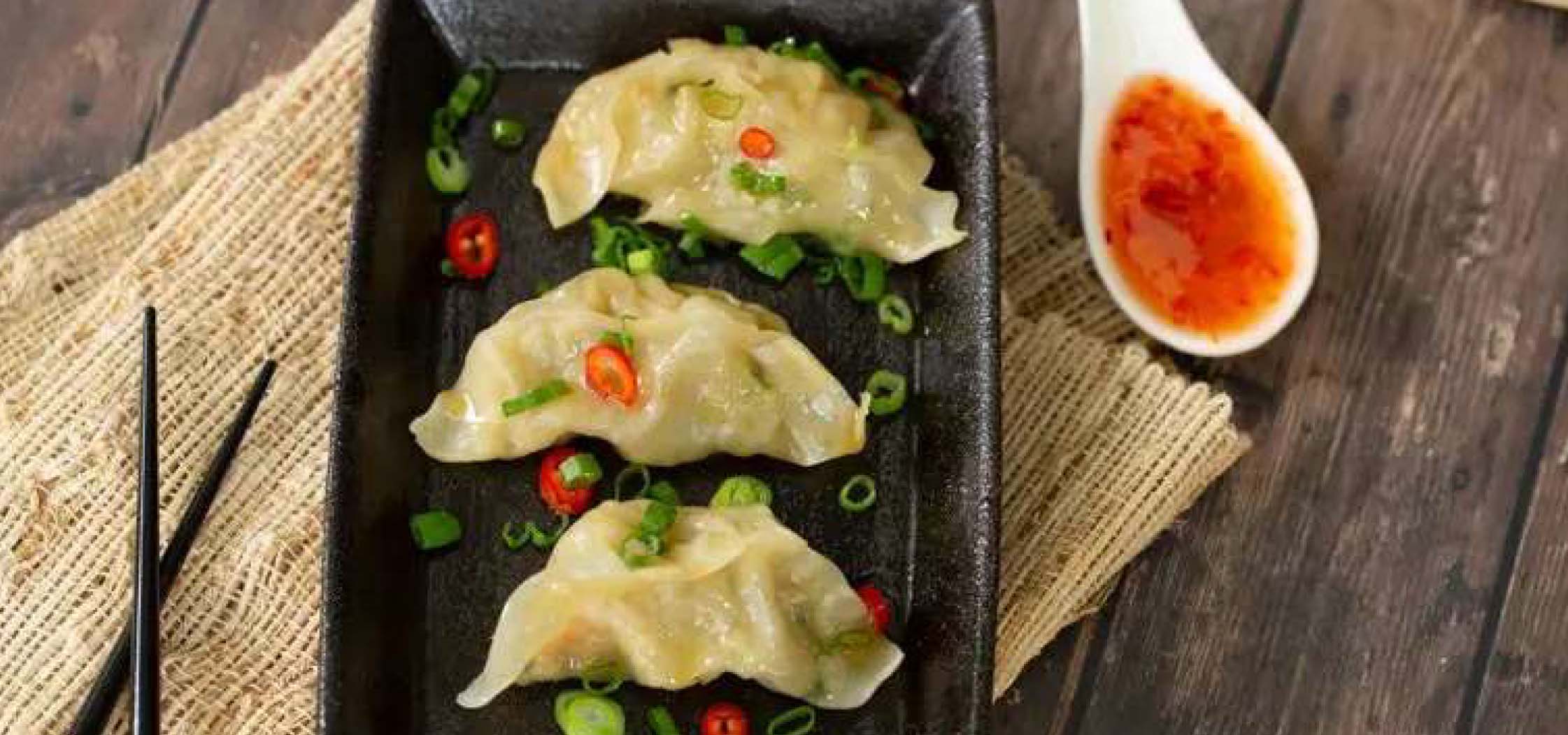 Three shrimp dumplings on a plate with a spoon of sweet chili sauce on the side.